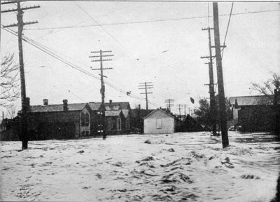 Man walking along the telephone cables after escaping from his house, which was washed away by the flood. The houses in the center have been washed from their foundations and are floating away