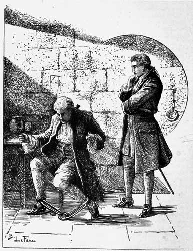 A man standing over another man who is chained to a chair.